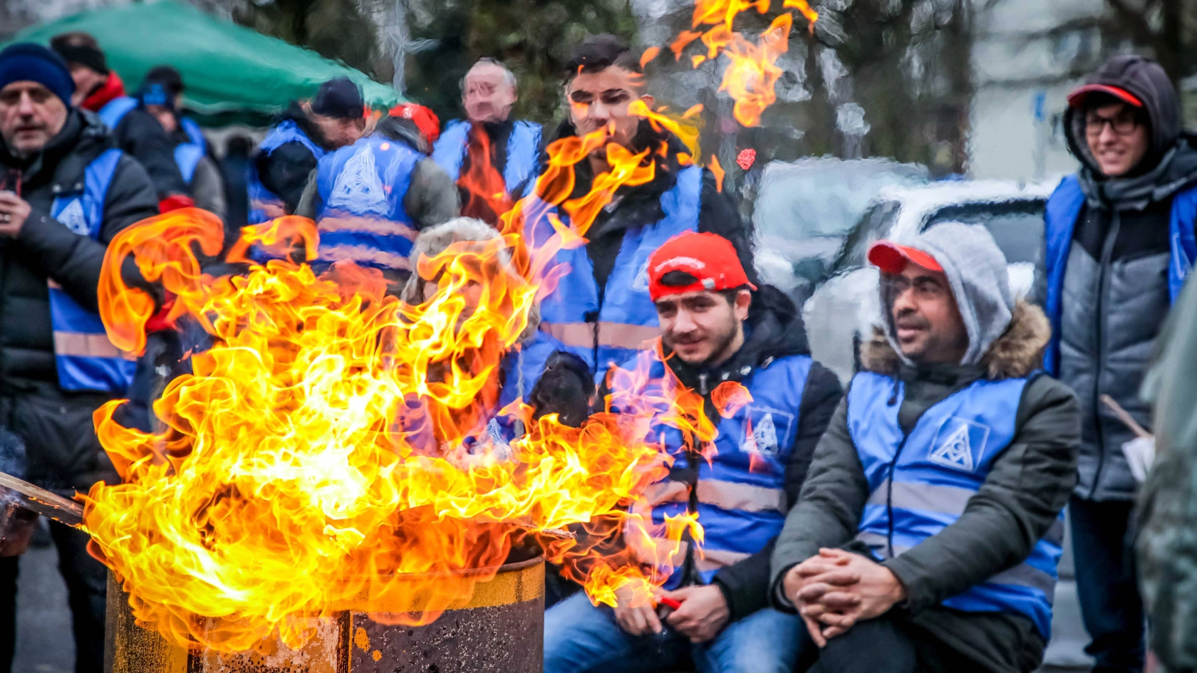 Mehrere junge Männer sitzen an einer Feuertonne.