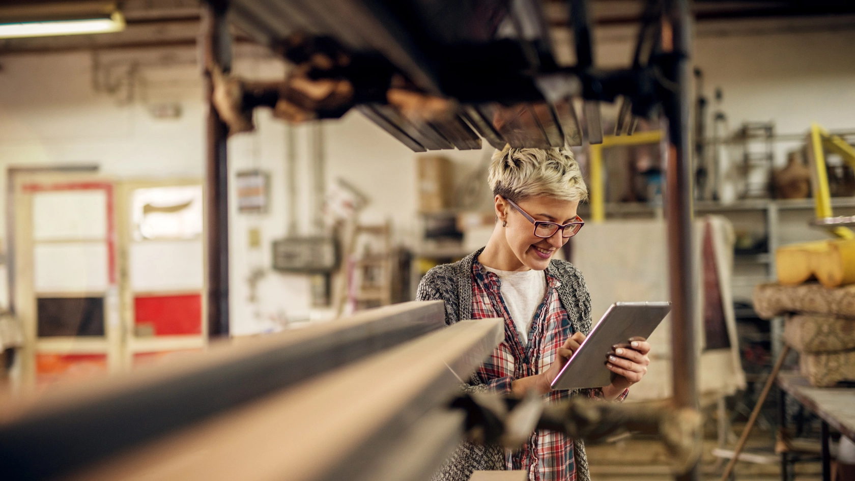 Junge Frau in der Werkstatt bedient ein Tablet.