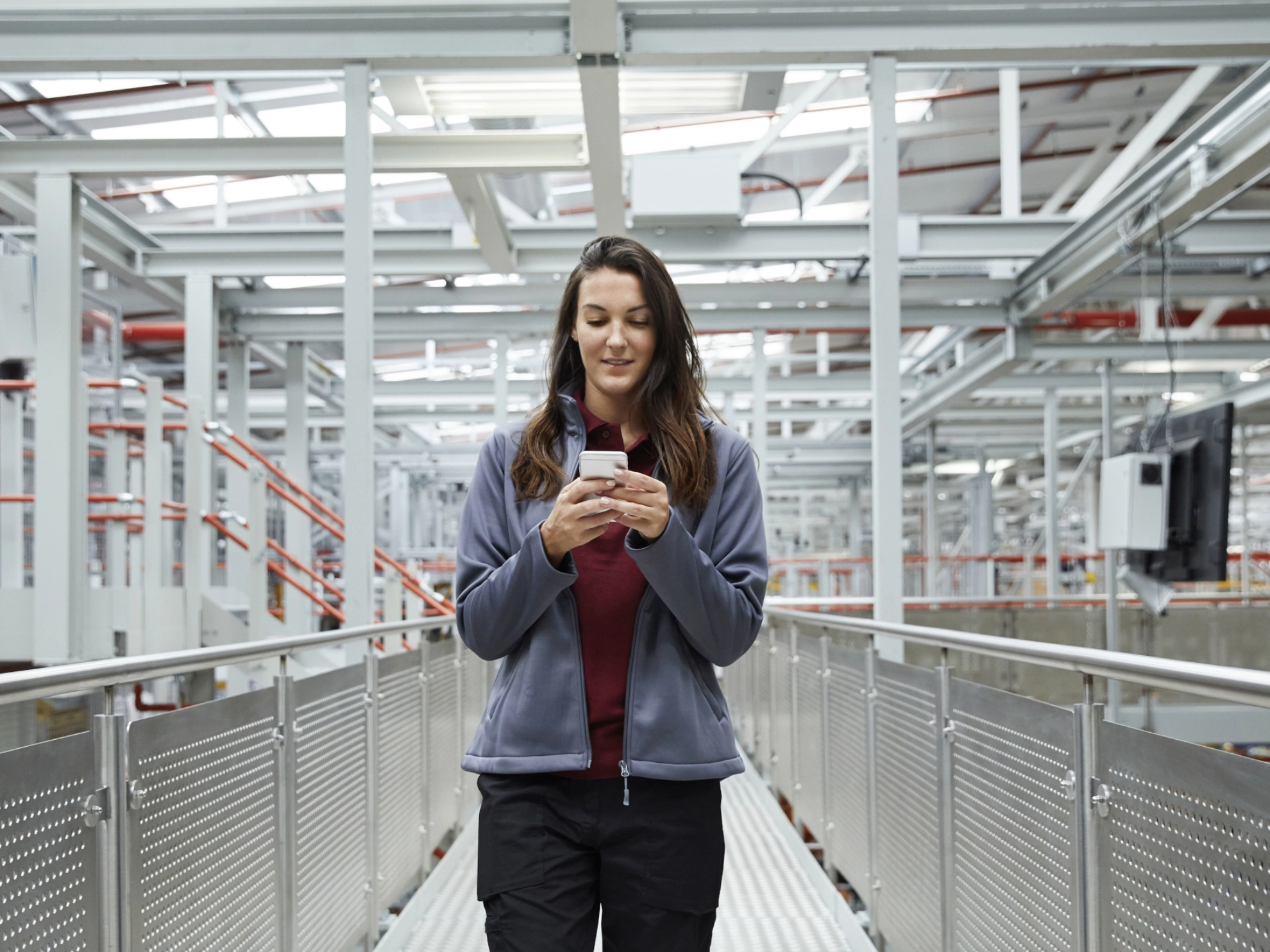 Eine junge Frau in Arbeitskleidung blickt auf ein Smartphone.