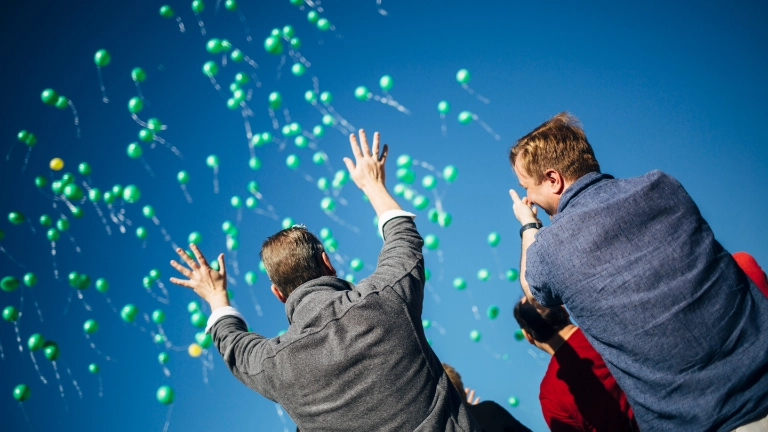 Zwei Menschen mit grünen Luftballons_Symbolbild